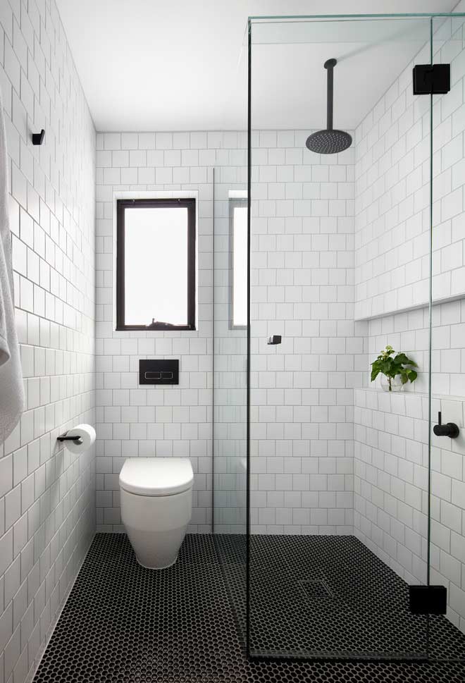 Um banheiro preto e branco com pastilhas retangulares e chuveiro de teto para dar um toque mais industrial.