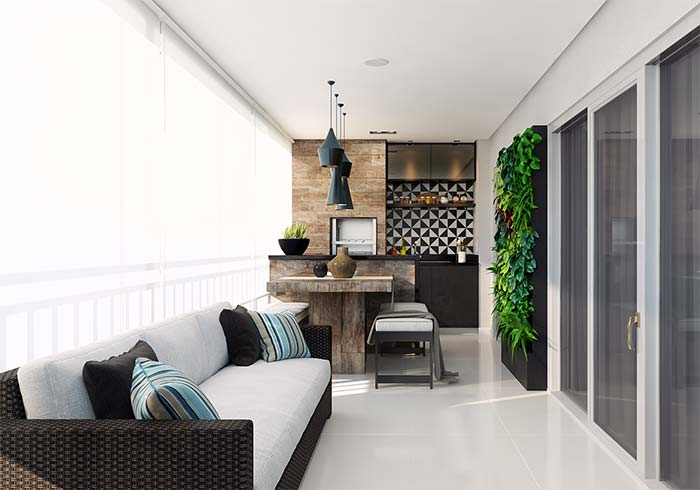 Varanda gourmet de apartamento com jardim vertical; o sofá longilíneo acompanha a extensão do ambiente.